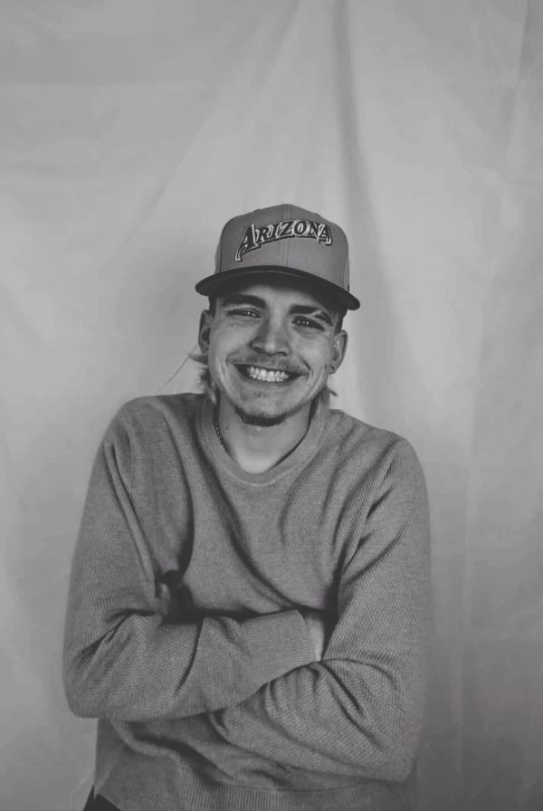 Young man smiling warmly, wearing an Arizona cap and cozy sweater.