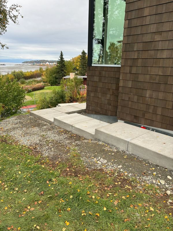 Concrete steps leading up to a modern house with a scenic view of trees and water.