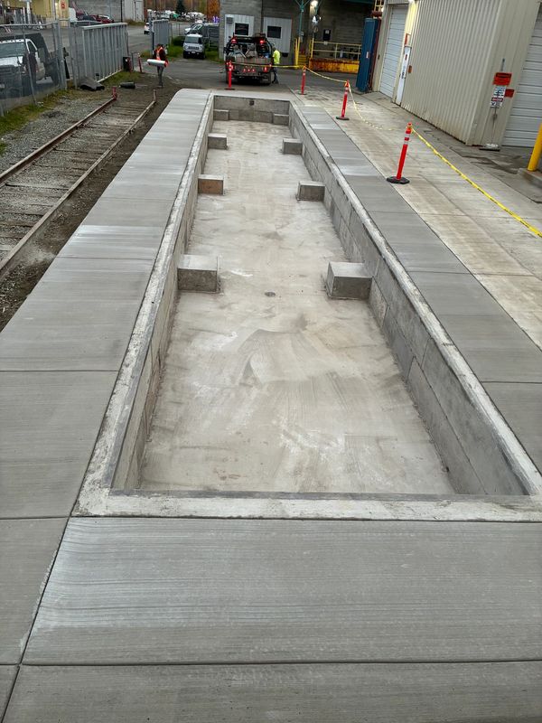 Empty concrete inspection pit with surrounding sidewalk at an industrial site.