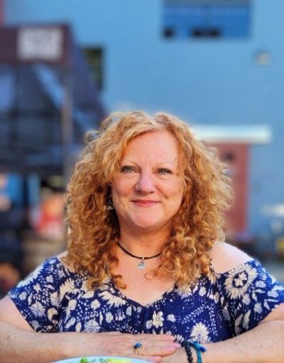 Smiling woman with curly red hair in a blue floral top.