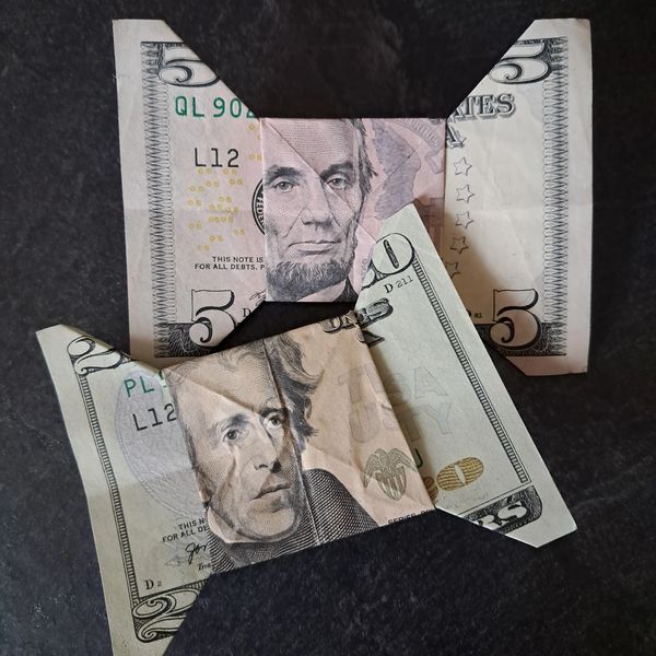 Two folded US dollar bills resembling animals on a dark surface.