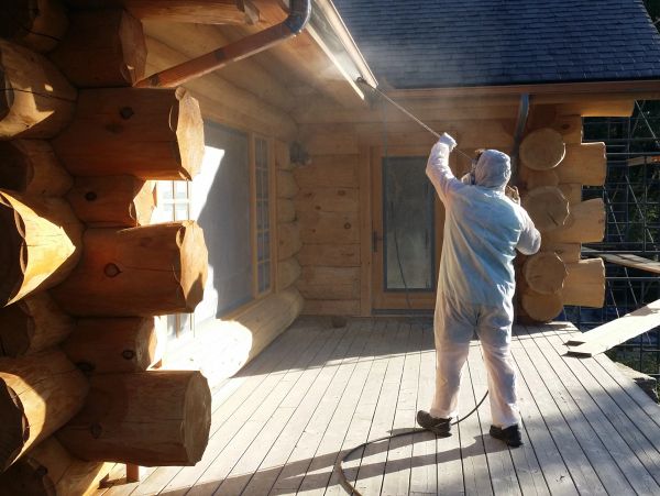 Person sprays a wooden log house with a hose.