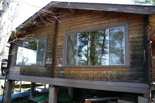 Wooden cabin with large windows and tree reflections.