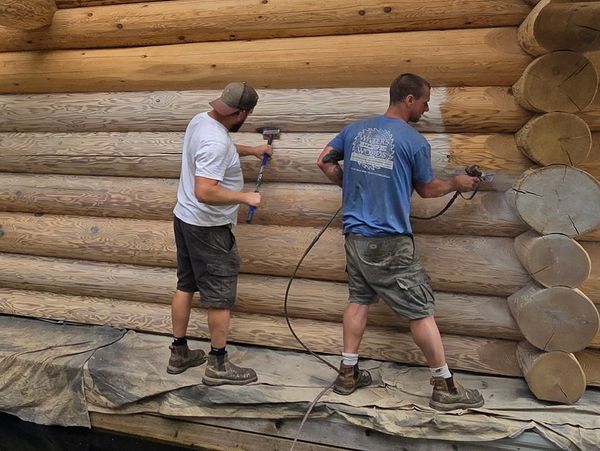 Two men working on a log cabin wall.