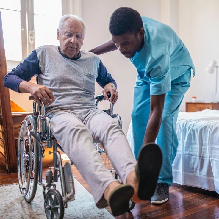 Caregiver assists elderly man in wheelchair inside a room.