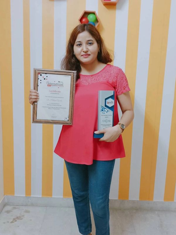 Woman in red top holding an award and certificate, standing against a striped yellow and white wall.