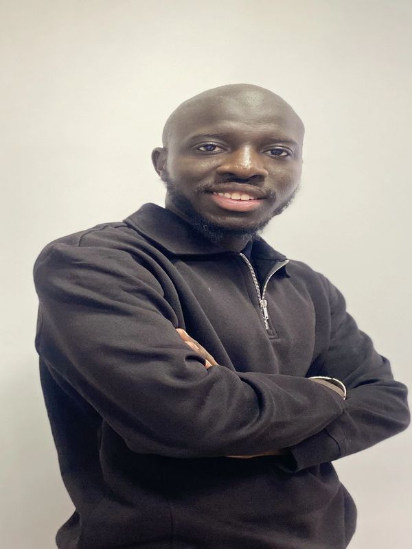 Confident man in a black zip-up sweater smiling with arms crossed against a plain background.