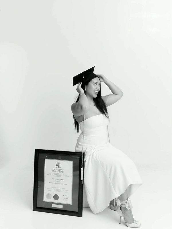 A woman in a white dress and graduation cap poses with a framed diploma.