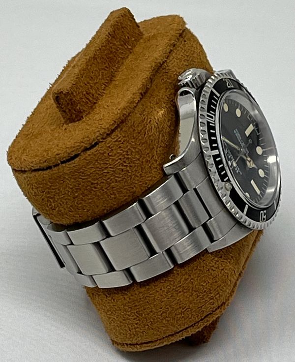 Stainless steel wristwatch with black dial on brown cushion.