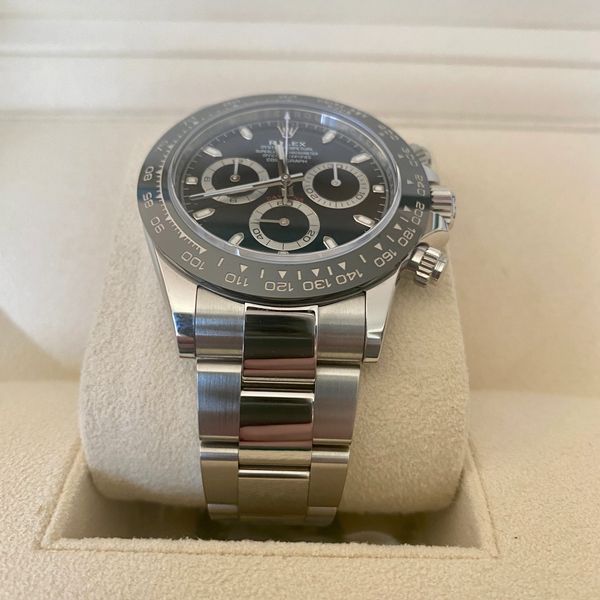 Close-up of a luxury Rolex Daytona watch with a black dial on a beige cushion.