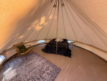 Cozy glamping tent interior with a bed, chair, and rug.
