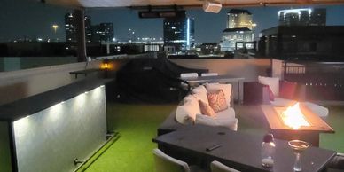 Cozy rooftop lounge with fire pit and city night view.
