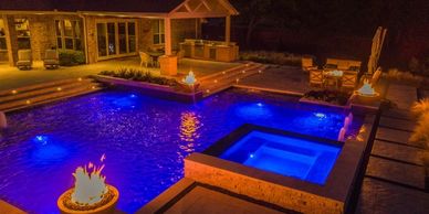 Luxury outdoor pool and spa area illuminated with blue and warm lighting at night.