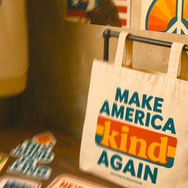 A tote bag with the message 'Make America Kind Again' displayed in a cozy shop.