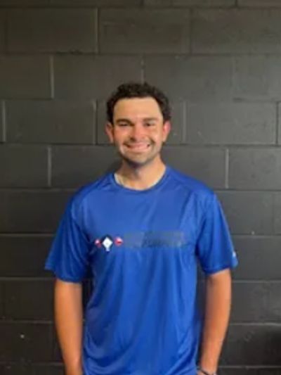 Young man smiling in a blue sports shirt against a black brick wall.
