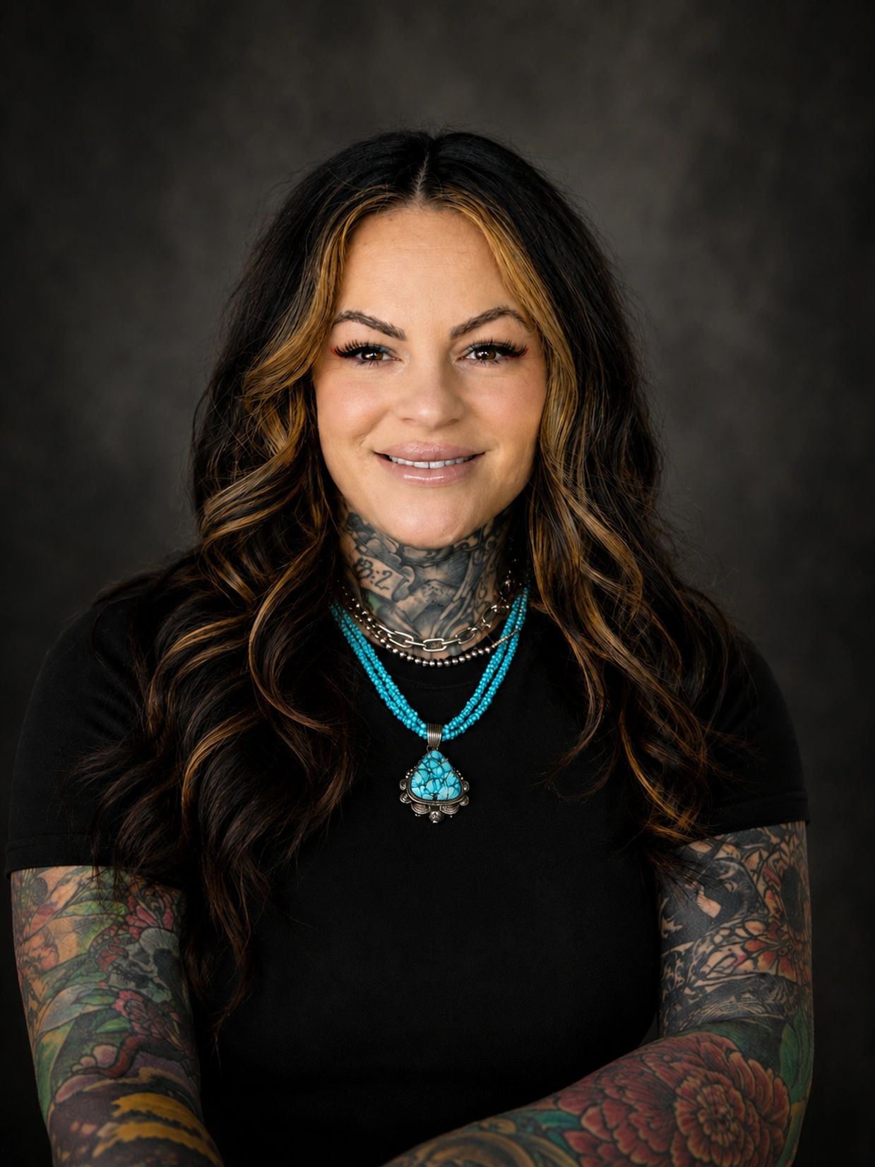 Smiling woman with tattoos and turquoise necklace.