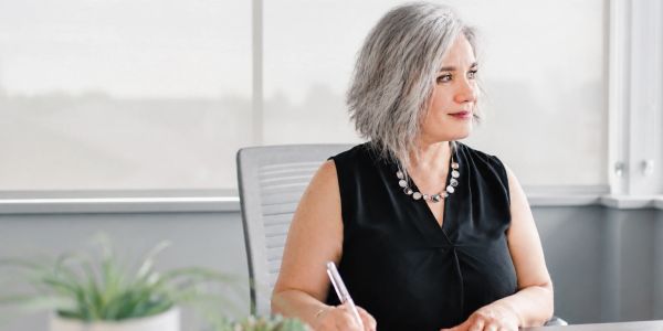 Woman with gray hair sitting at a desk looking thoughtful.