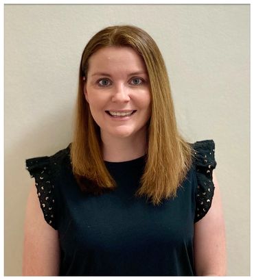 Smiling woman with straight light brown hair wearing a black top with ruffled sleeves.