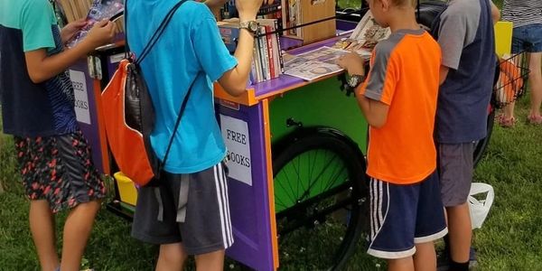 4 boys gathered around a book bike, choosing something to read. 