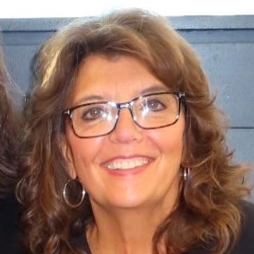Smiling woman with glasses and wavy hair.