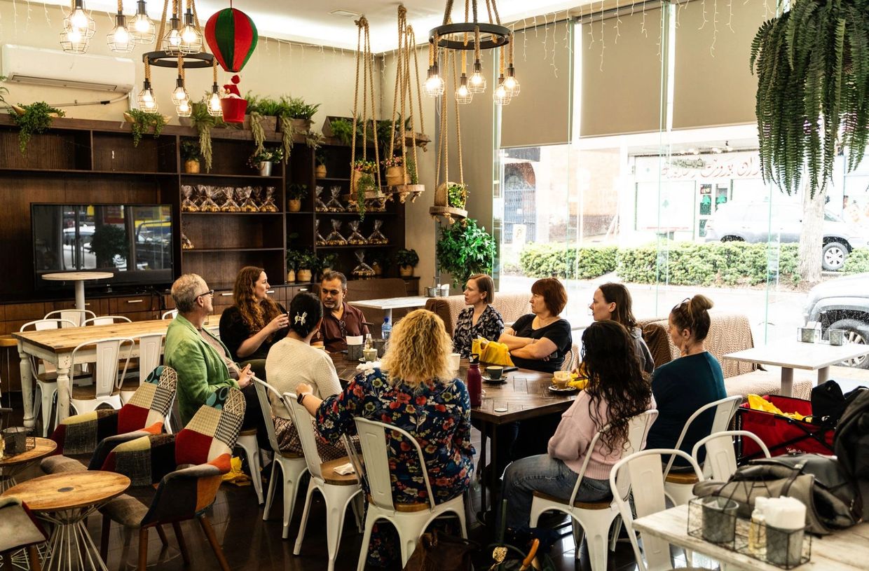 Group of people having a discussion in a cozy cafe with hanging plants and warm lighting.