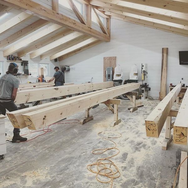 Woodworkers shaping large wooden beams in a bright, spacious workshop.