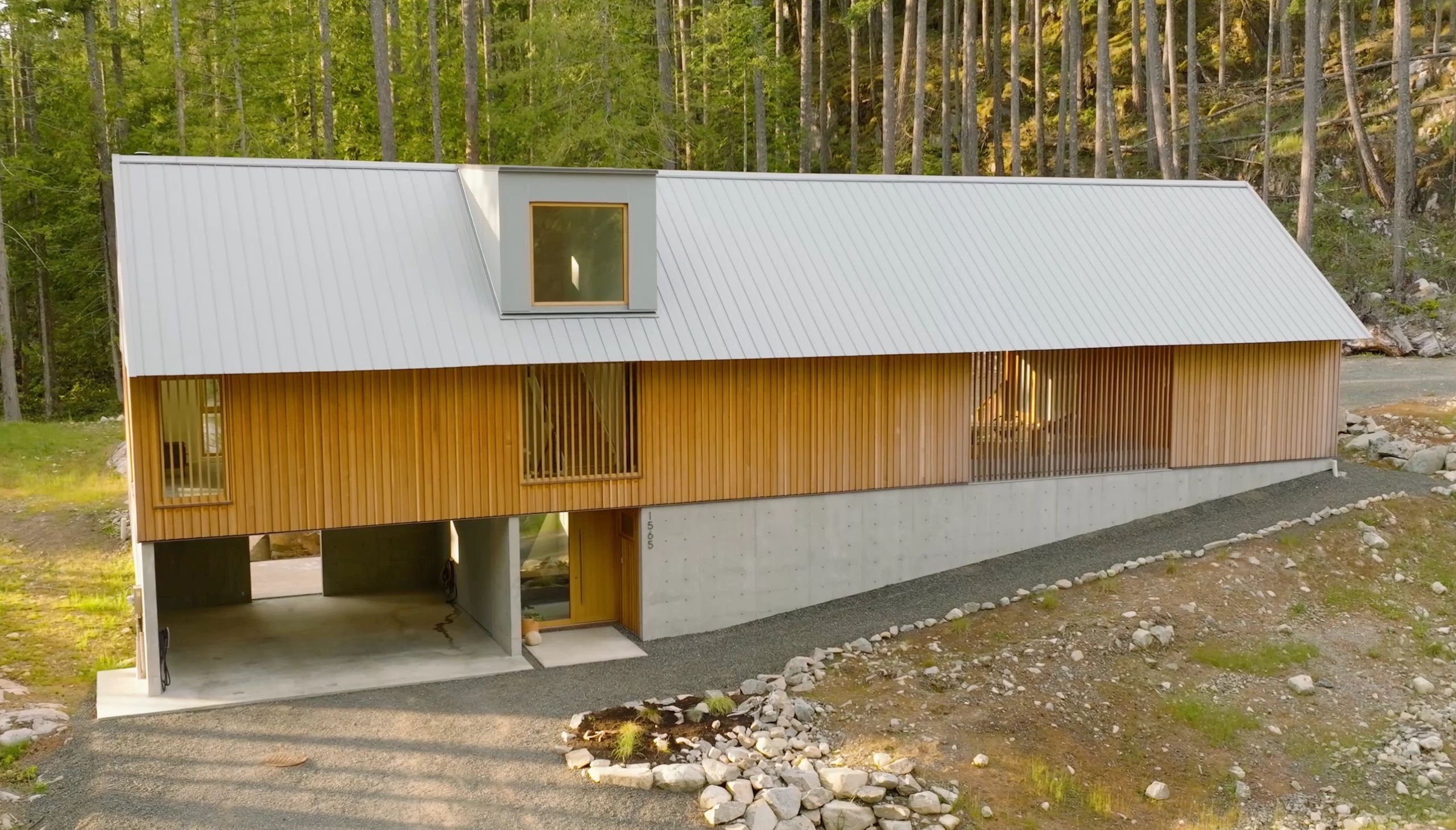 Modern wooden house with a gray metal roof in a forested area.