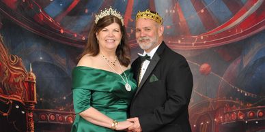 A couple dressed in formal attire wearing crowns and smiling.
