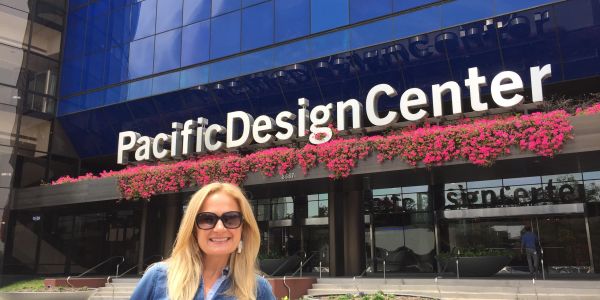 A woman smiling in front of the Pacific Design Center with pink flowers above the sign.