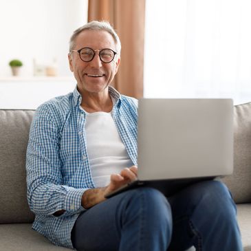 Happy elderly man sitting on coach with open laptop