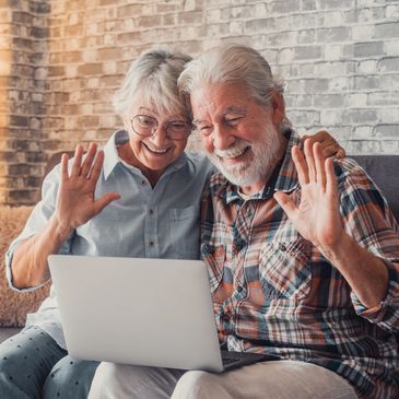 Happy Elderly couple sitting on a lounge waving at an open laptop 