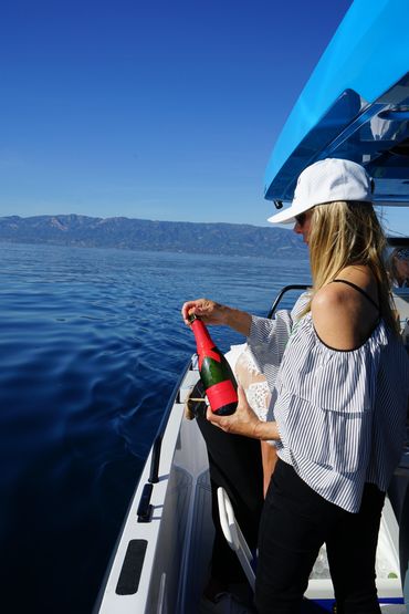 Woman holding a champagne bottle on a boat with calm water and mountains in the background.