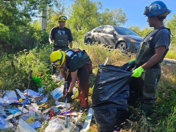 Three workers cleaning up trash outdoors.