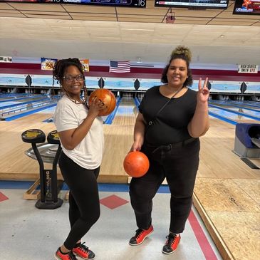 Two women holding bowling balls at a bowling alley.