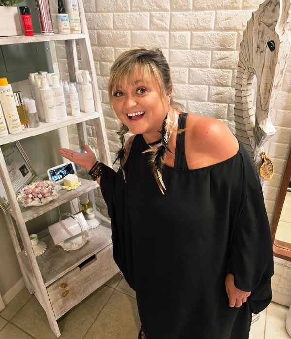 Smiling woman in black dress showing beauty products on a shelf.