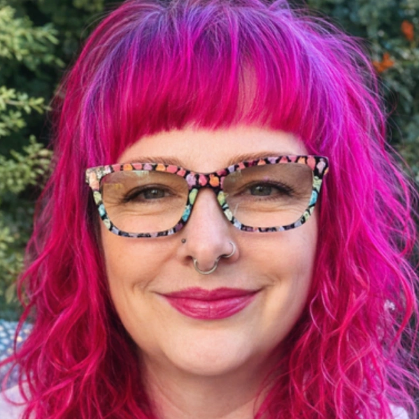 Woman with vibrant pink hair and colorful glasses smiling outdoors.