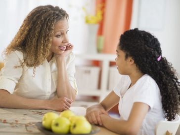 Woman attentively listening to a girl at the kitchen table.