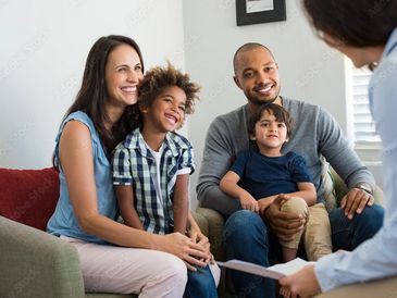 A happy family of four talking with a professional in a cozy living room.