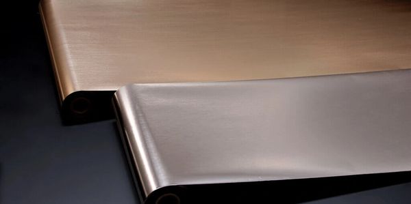 Two rolls of metallic foil in bronze and silver hues on a dark surface.