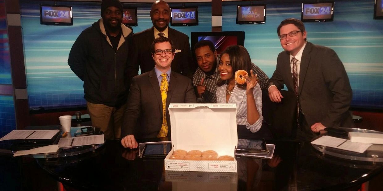 News team at FOX24 smiling with a box of donuts on the desk.