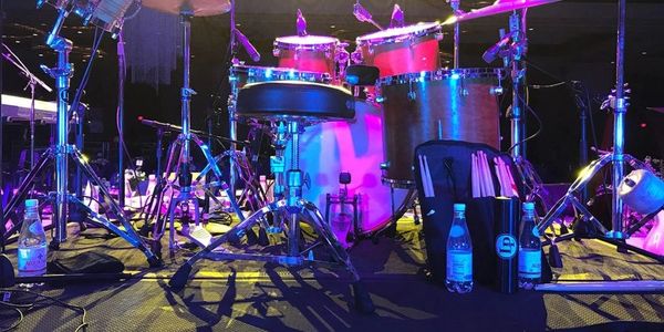A colorful drum kit set up on a stage with bright lights and water bottles.
