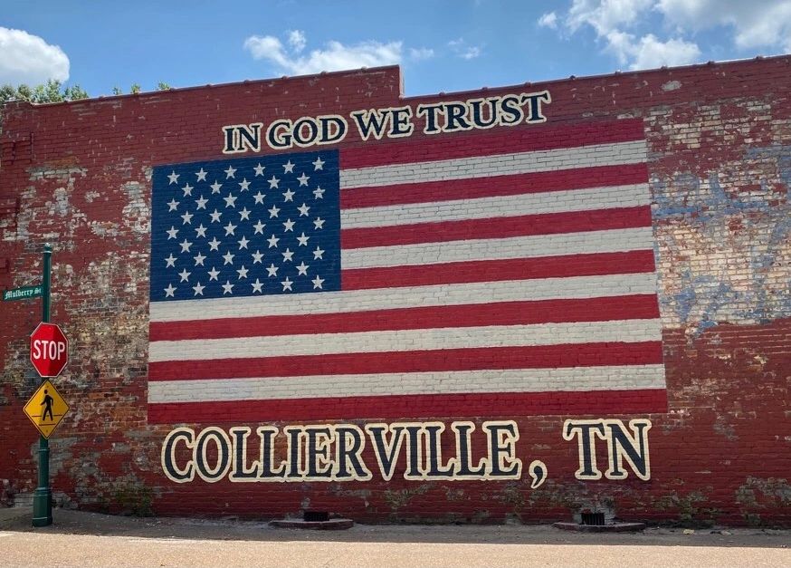 Mural of American flag with 'In God We Trust' and 'Collierville, TN' painted on brick wall.