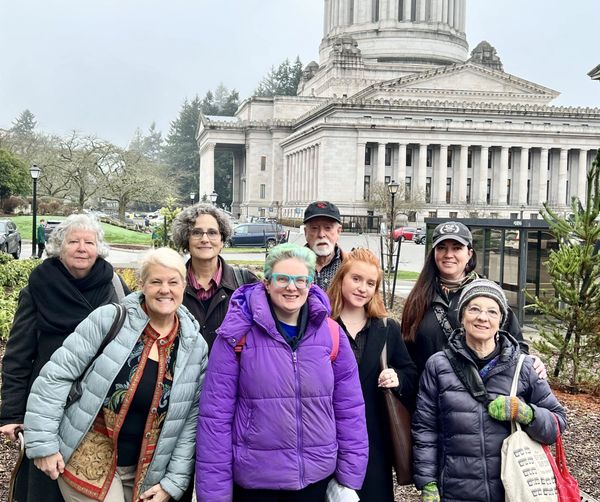 Group of eight people posing outside a large government building in winter clothing.