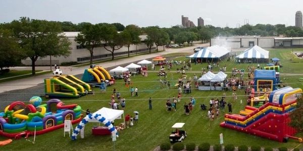A community event with colorful inflatable slides and tents on a grassy field.