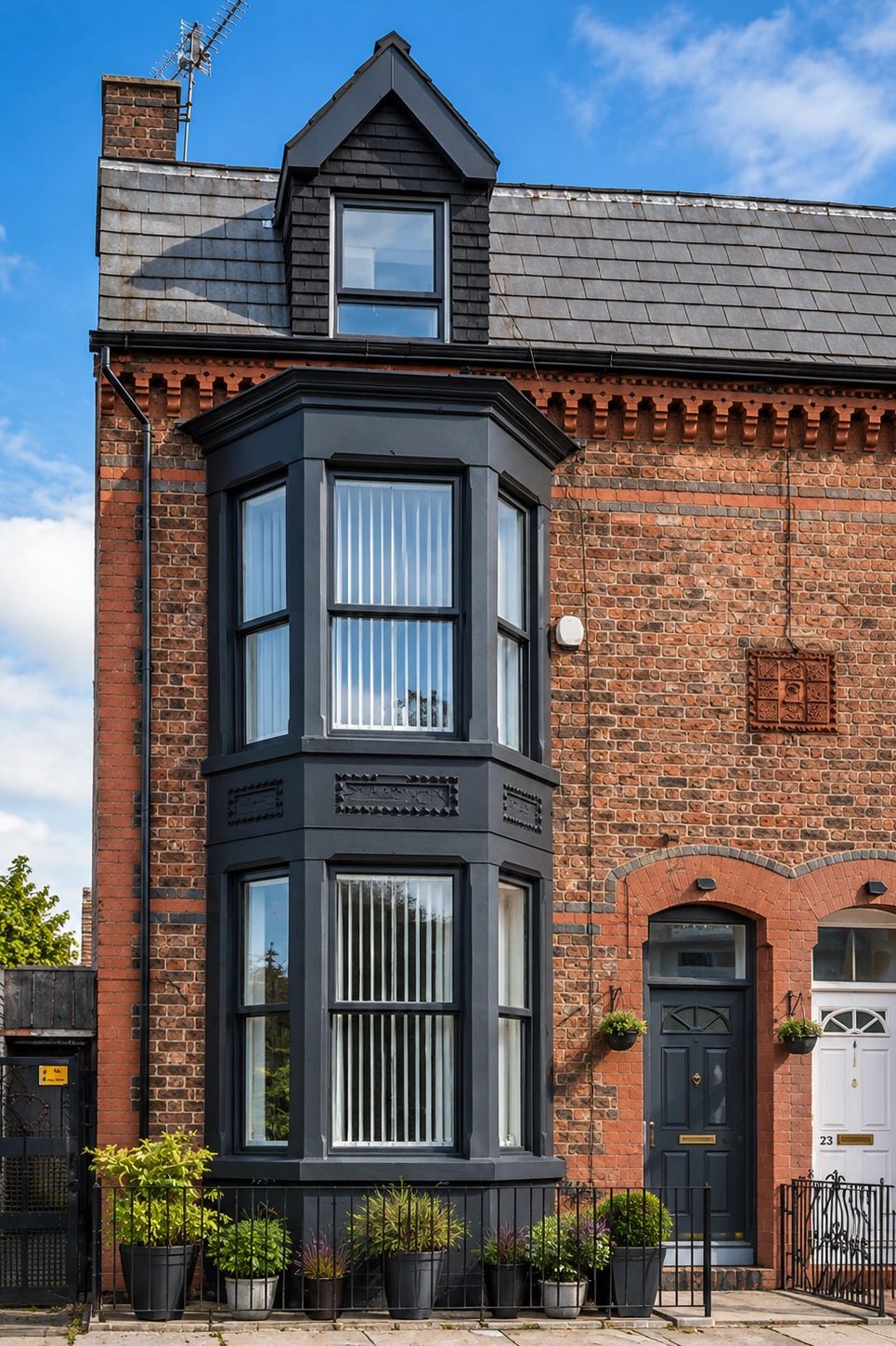 Brick house with dark bay windows and potted plants.
