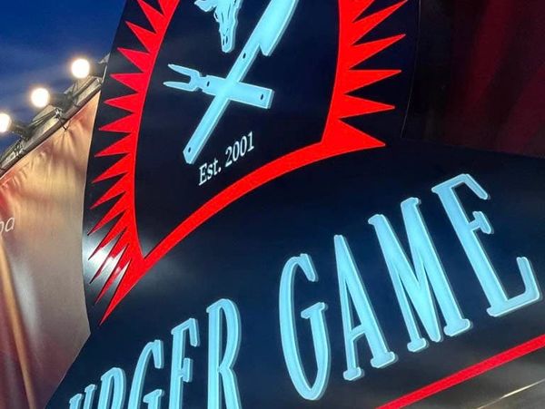 Close-up of a bright restaurant sign with grilling tools and establishment year.
