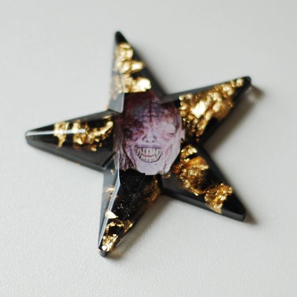Black star-shaped object with gold flakes and a creepy face in the center.