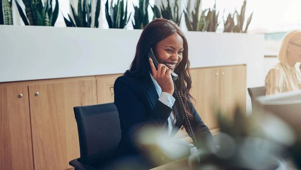 Smiling woman in business attire talking on the phone at her desk.