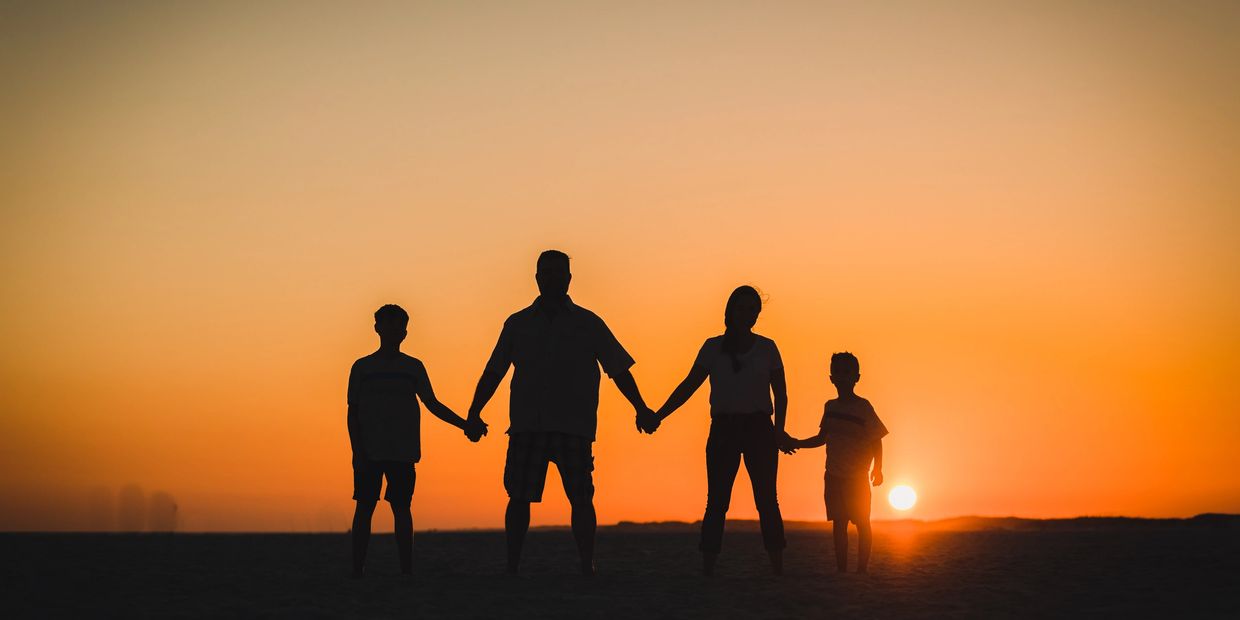 Silhouetted family holding hands at sunset on the beach.