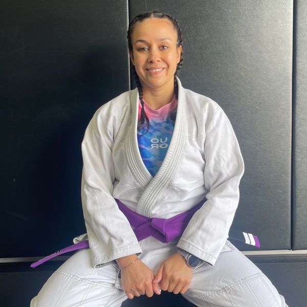Smiling woman in a white martial arts gi with a purple belt.